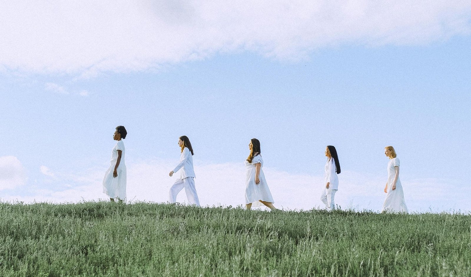 A group of women walking together across a green hillside under an open sky